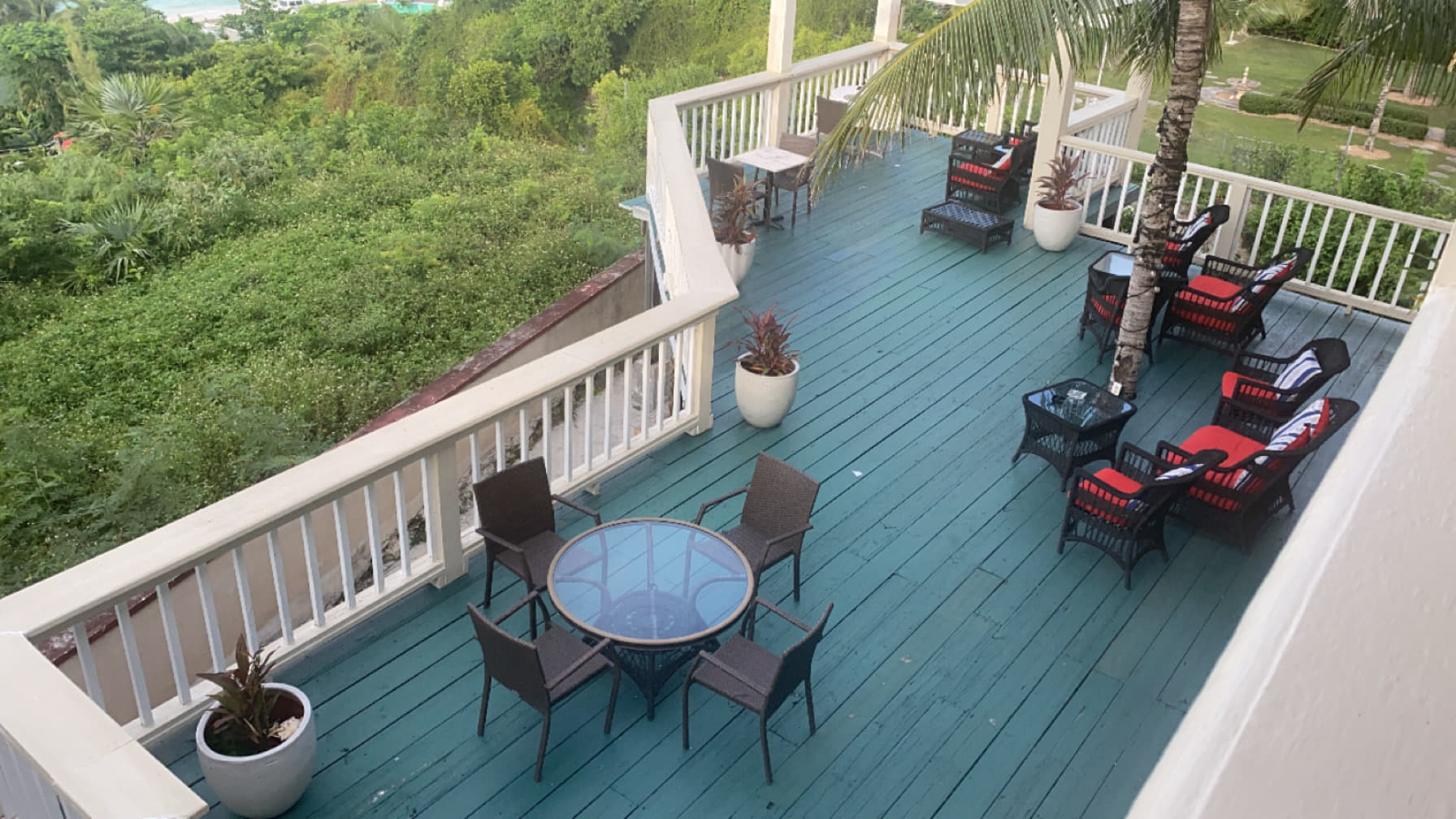 The wide upper deck furnished with wicker armchairs and low tables, greenery falling away below the rail