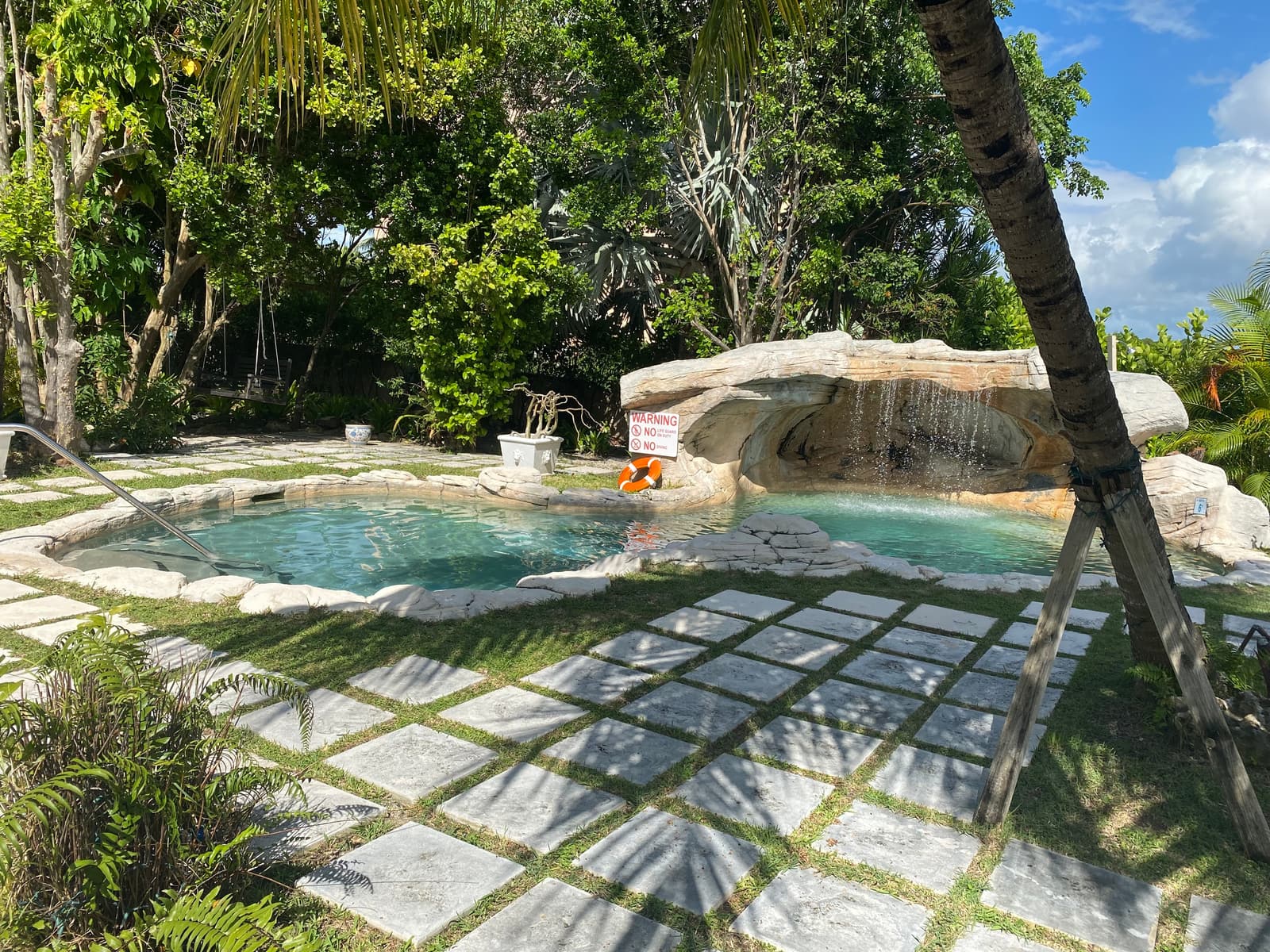 The pool's limestone waterfall, water sliding over pale rock into the shallow end beneath overhanging greenery