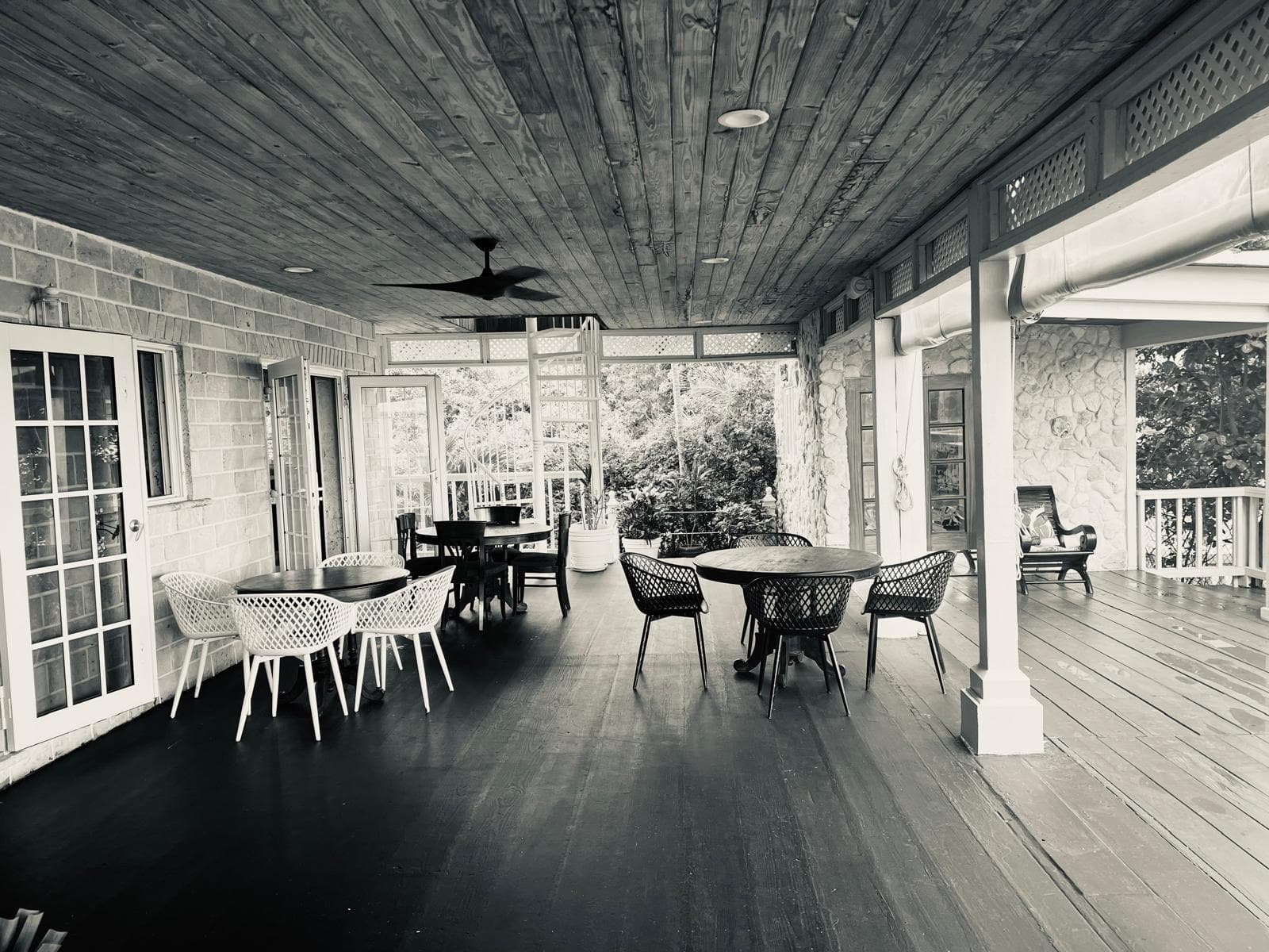 The long covered veranda set with round tables and slatted chairs beneath a wood ceiling and paddle fans